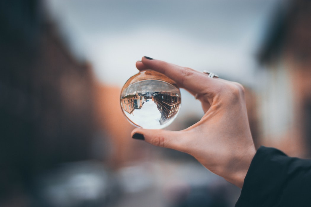Hand holding a lensball through which you can see a street view which has been flipped upside down through refraction