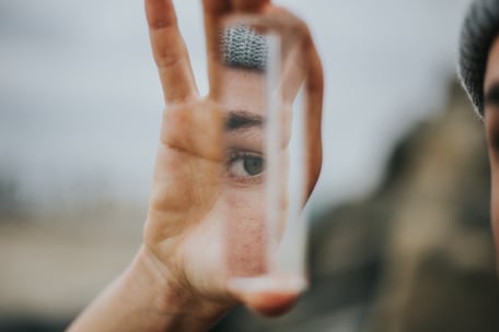 A human hand holding an upright rectangular prism through which a person's eye and eyebrow are shown