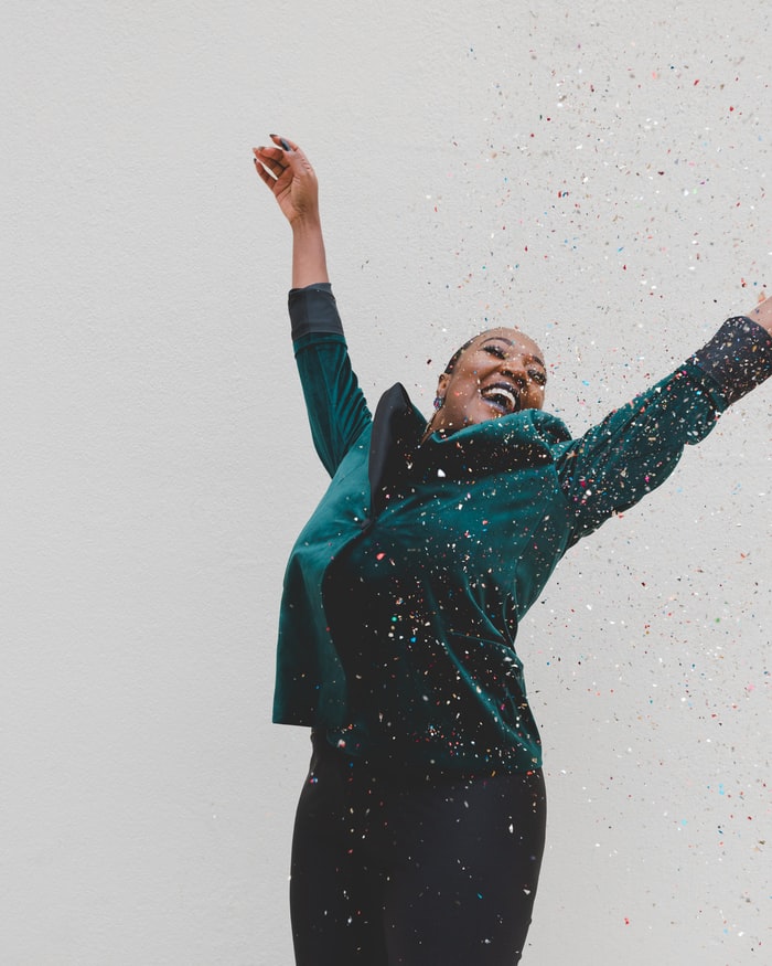 Woman in turquoise jacket with head thrown back and arms in the air and confetti raining down on her